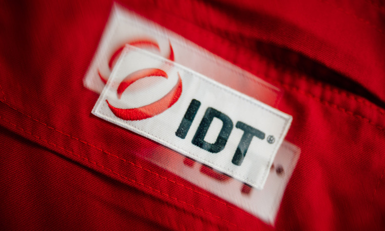 Weißer IDT-Schriftzug mit rotem Ring-Logo auf einem Aufnäher an einer roten Arbeitsjacke