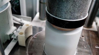 Weißer zylindrischer PTFE-Rohling in einer Presse, von oben mit einem metallischen Stempel verdichtet