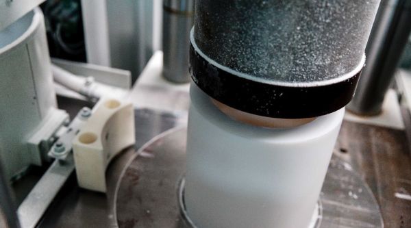Weißer zylindrischer PTFE-Rohling in einer Presse, von oben mit einem metallischen Stempel verdichtet