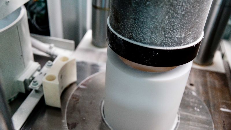 Weißer zylindrischer PTFE-Rohling in einer Presse, von oben mit einem metallischen Stempel verdichtet